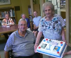 HAL TO CELEBRATE-- David MacMillan and Theodora Rose, two of the late Hal Smith's first cousins, display a custom cake as others look on during the party marking Hal's 100th birthday. Photo by John D. Michaud III.